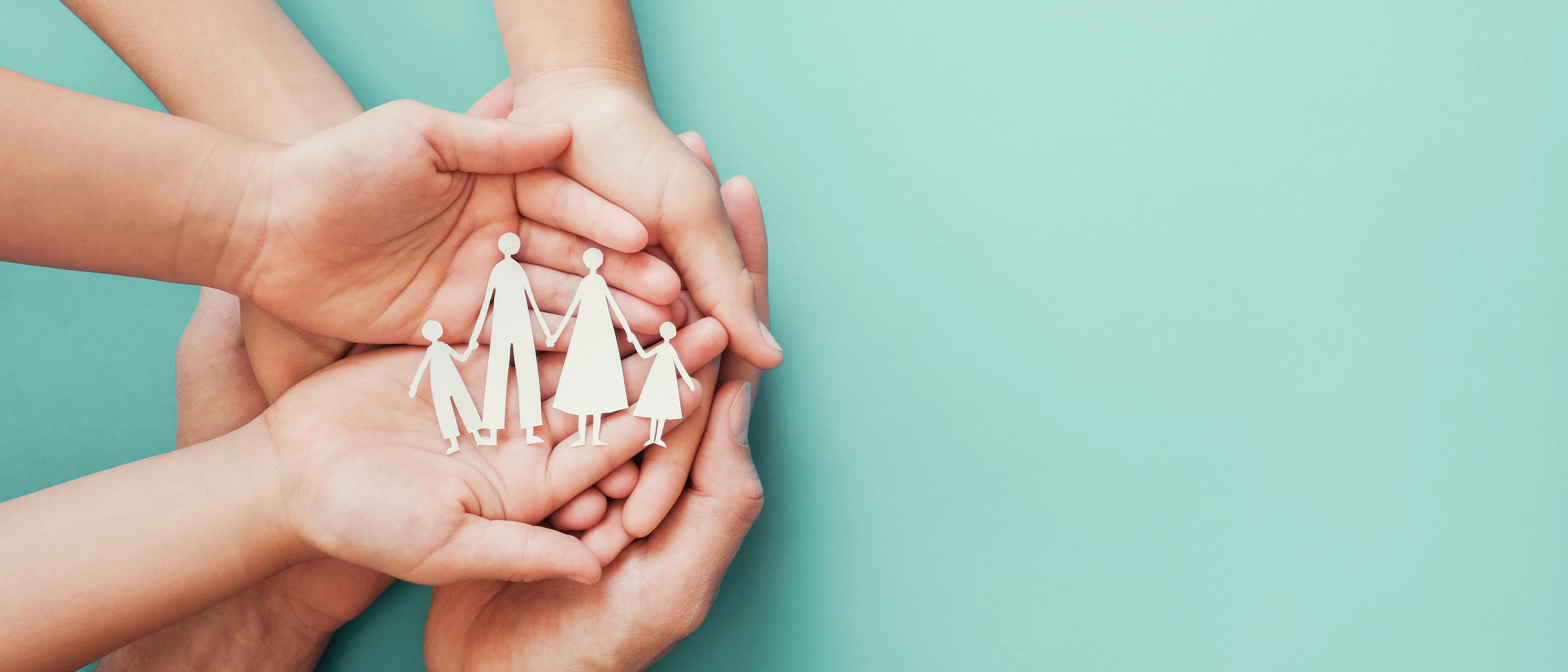Close-up of white paper cut-outs of a family being cradled in several people's hands 