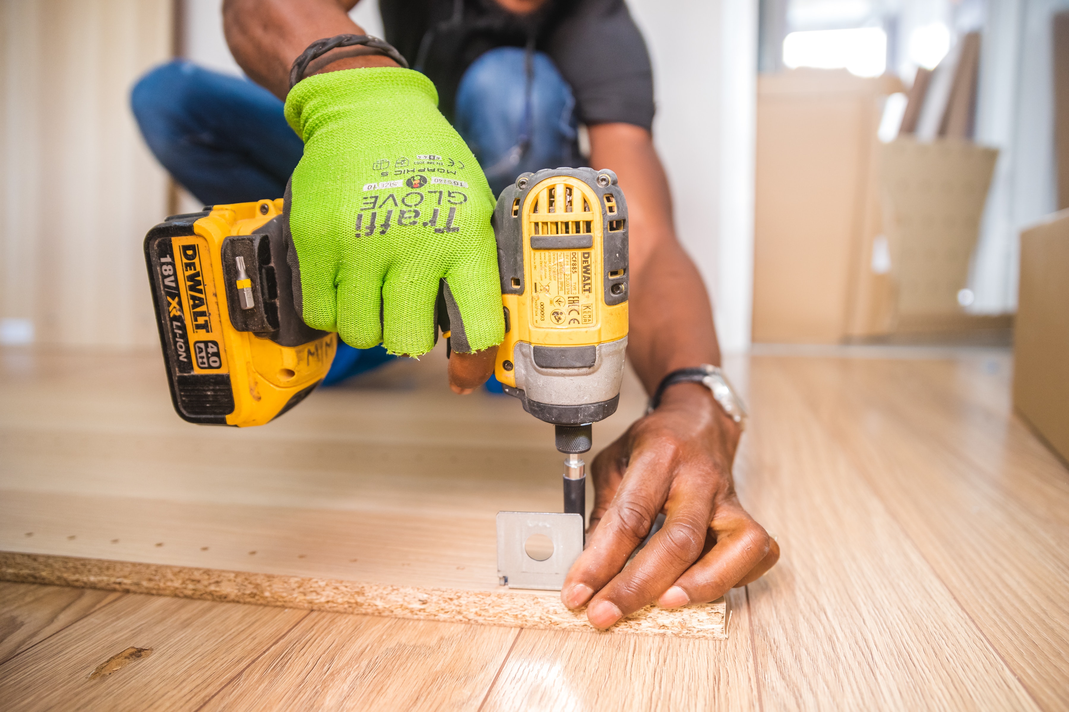 A close up on a person's hands using an electric screwdriver, attaching a metal bracket to a piece of wood.