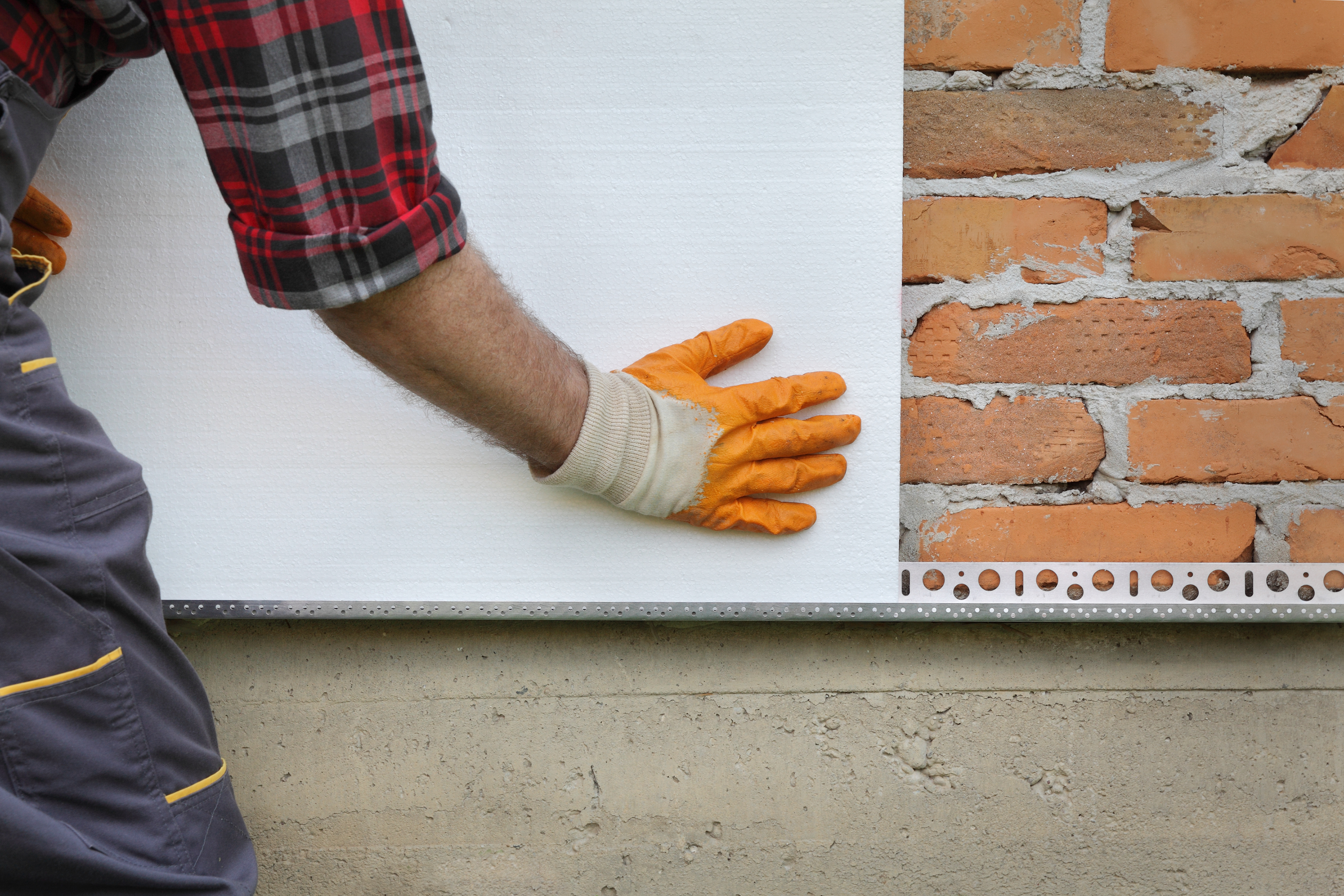 Close-up photograph of a construction worker fitting insulating board on a brick wall