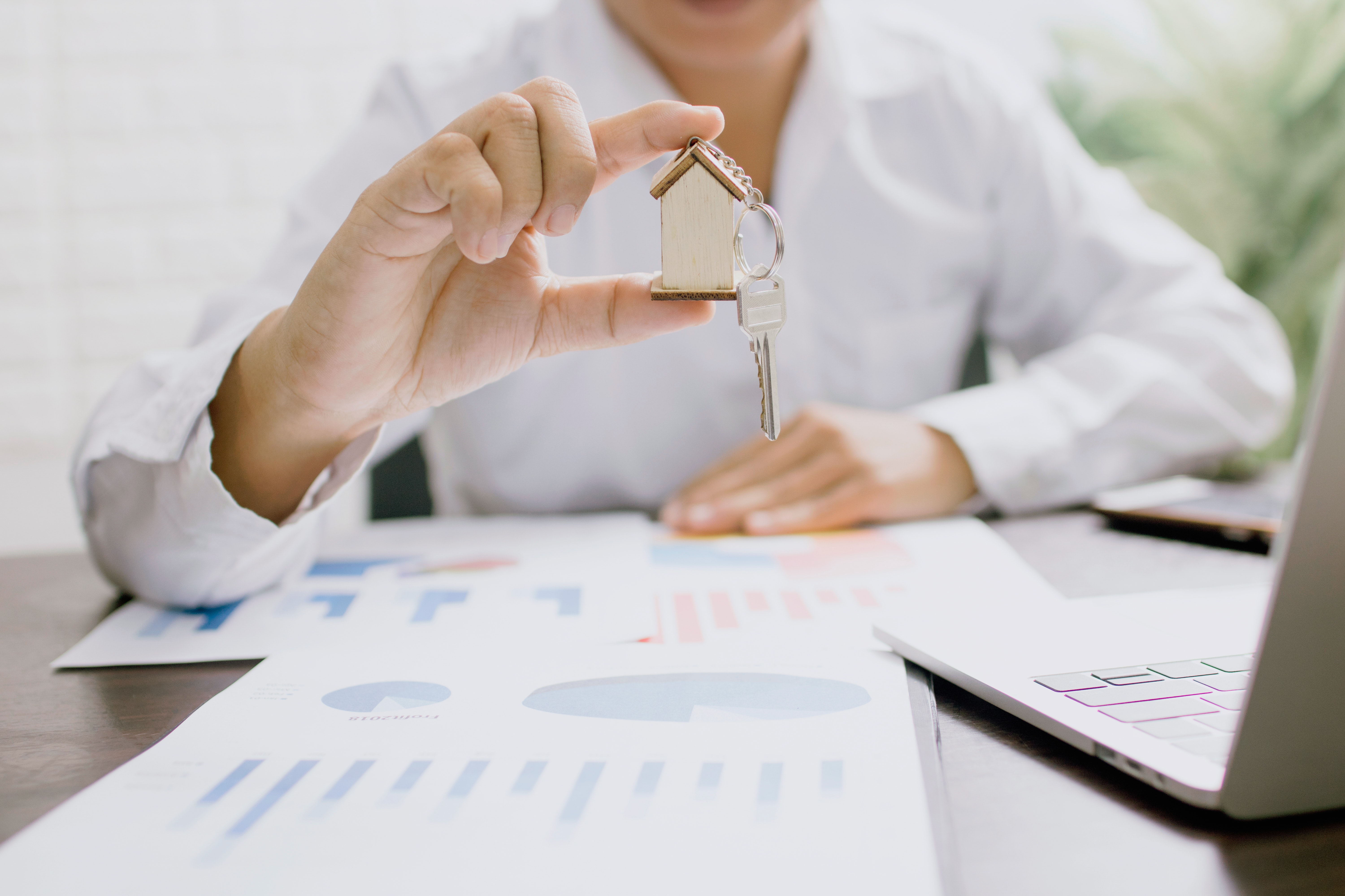 Photograph of someone holding a key with a house-shaped keyring over financial charts
