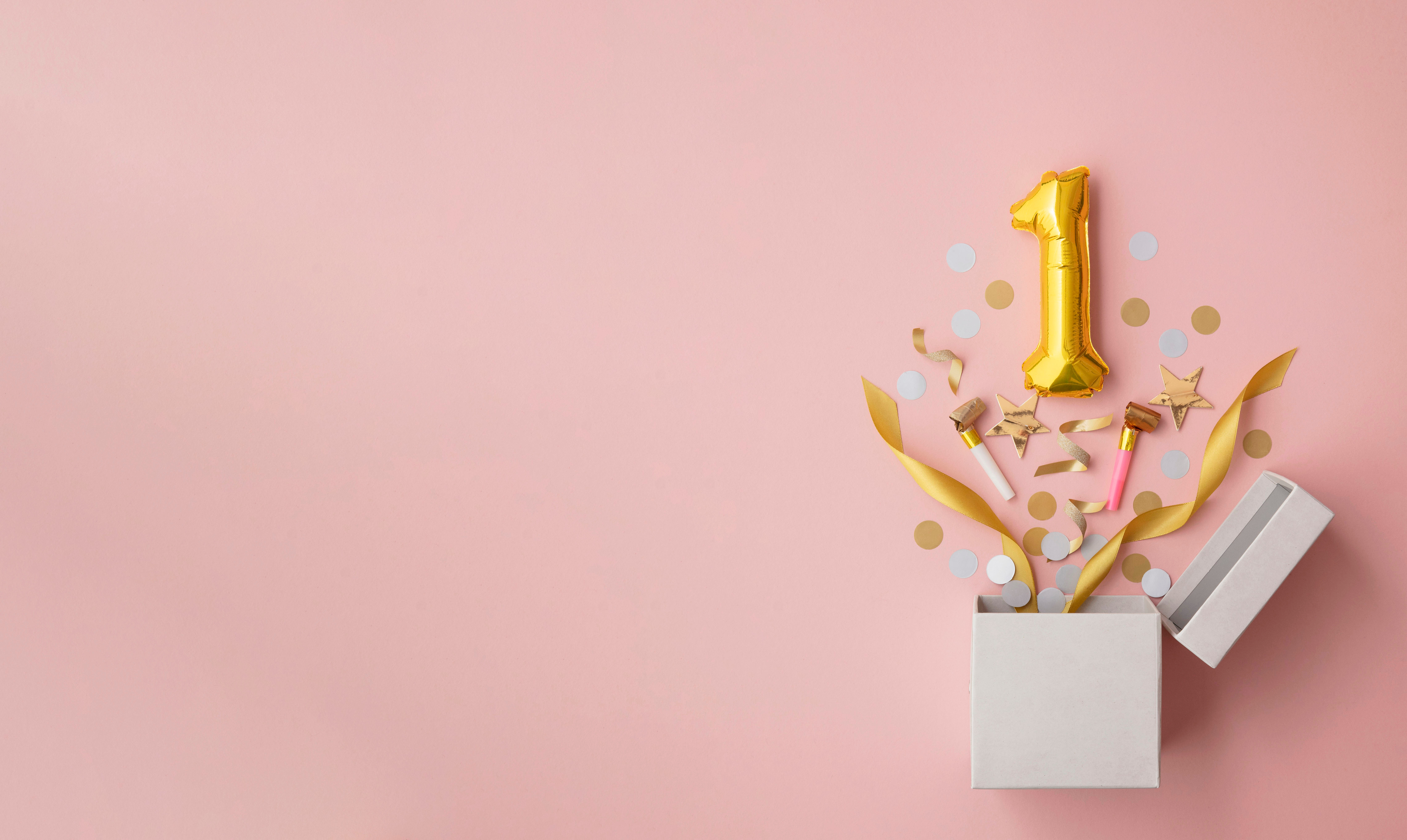 Photograph of a gold balloon in the shape of the number 1 popping out of a box together with ribbons and confetti