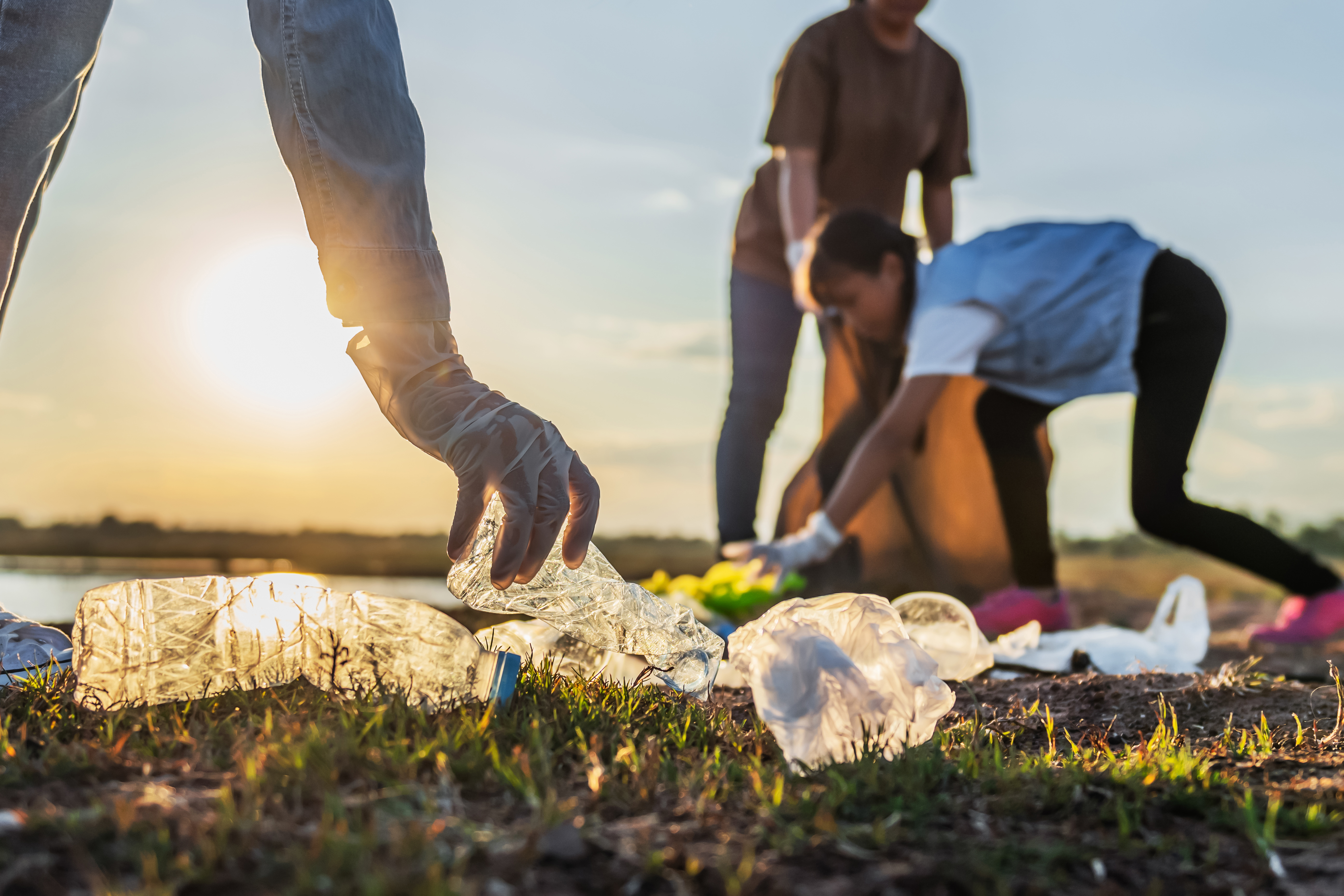 People Volunteer Keeping Garbage Plastic Bottle Into Black Bag Park Near River Sunset