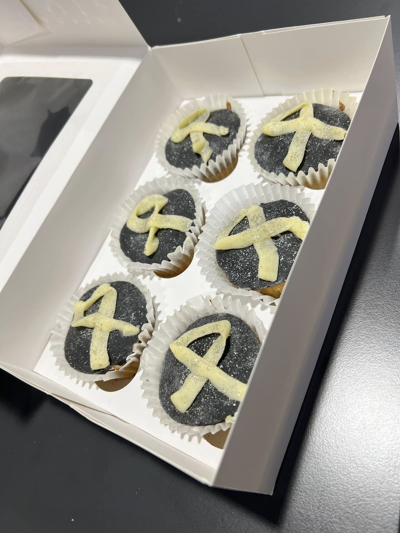 Photo of a box of cupcakes with a white ribbon iced on