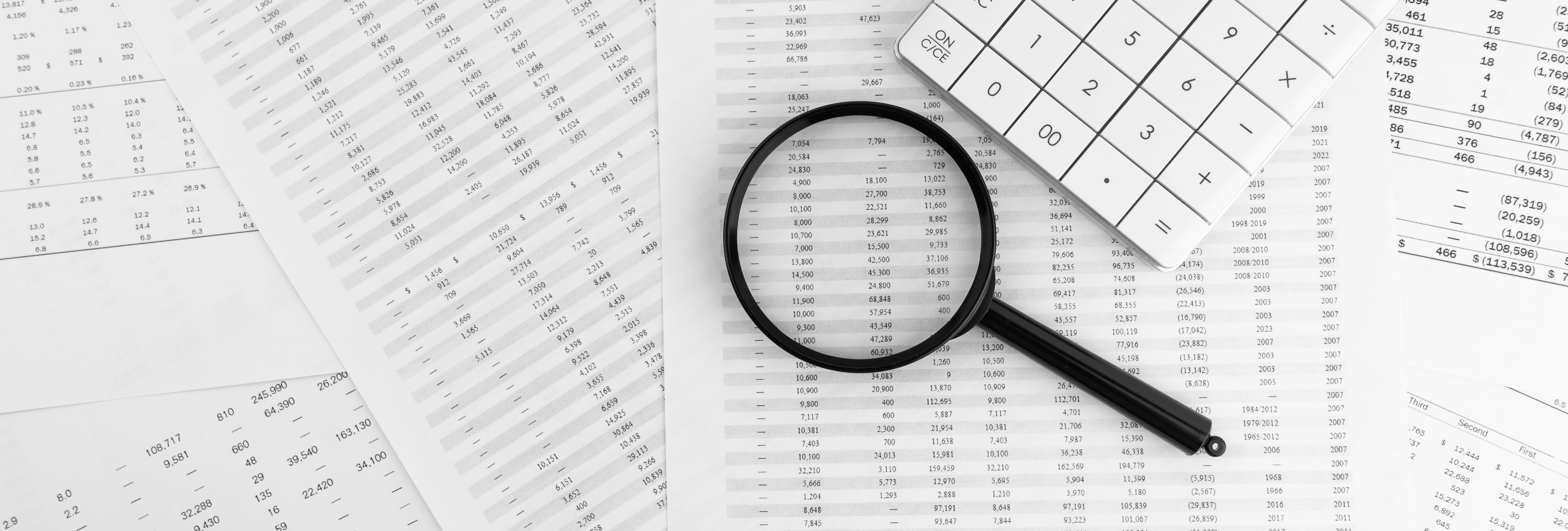 Magnifying glass and calculator sitting on top of printed spreadsheets spread out on a table