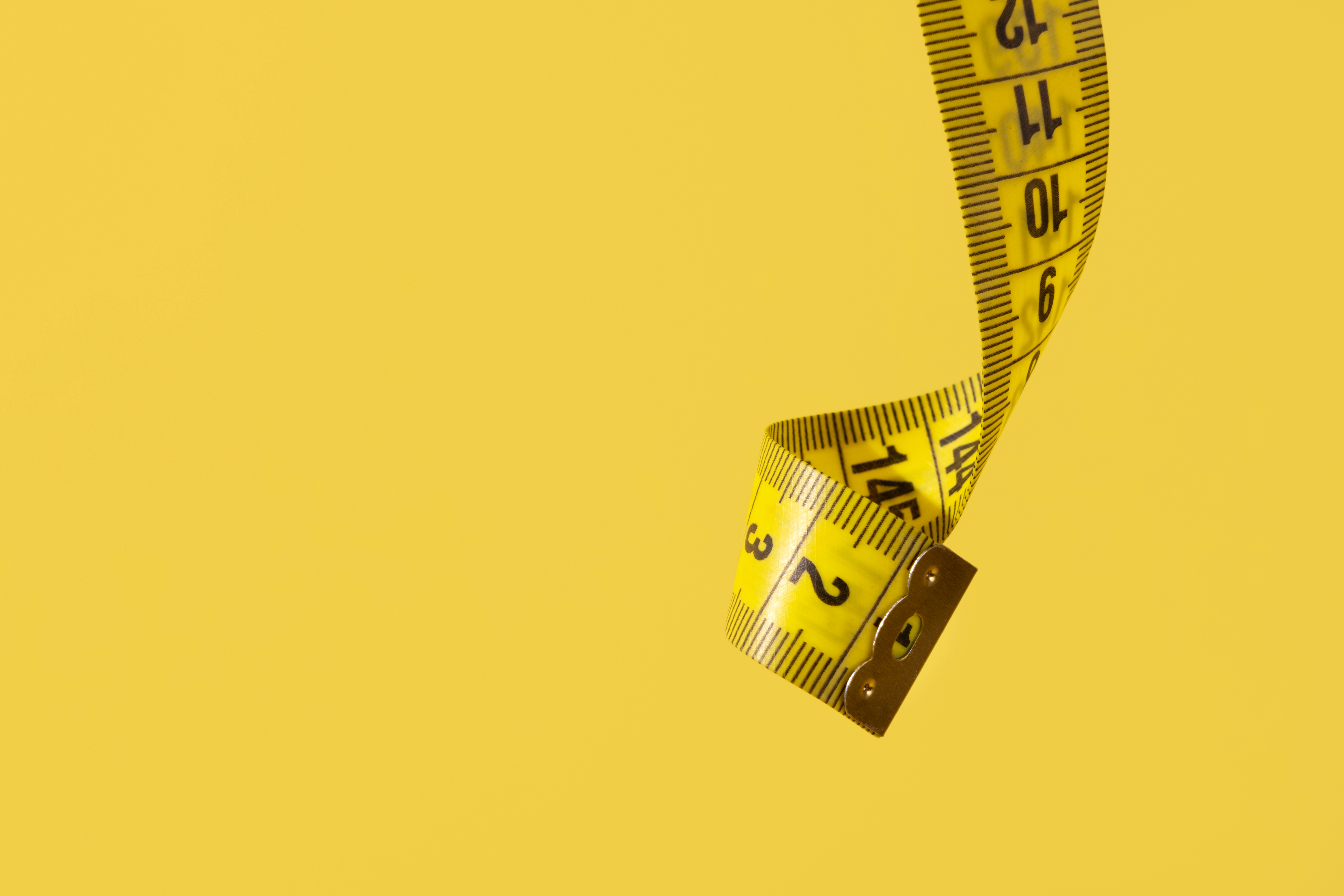 close-up photo of a yellow tape measure dangling down in front of a yellow background