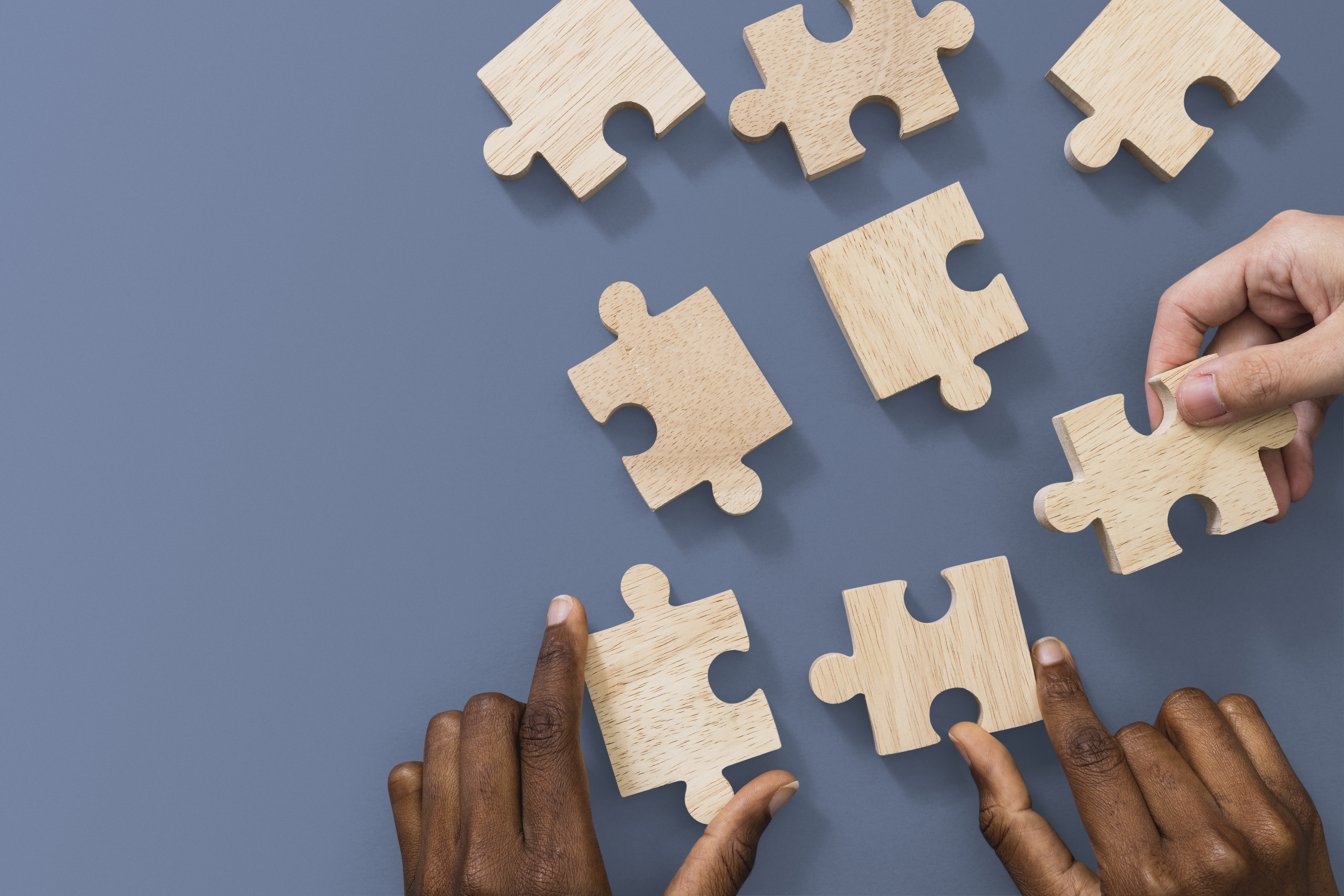 Wooden puzzle pieces with hands holding some of the pieces 