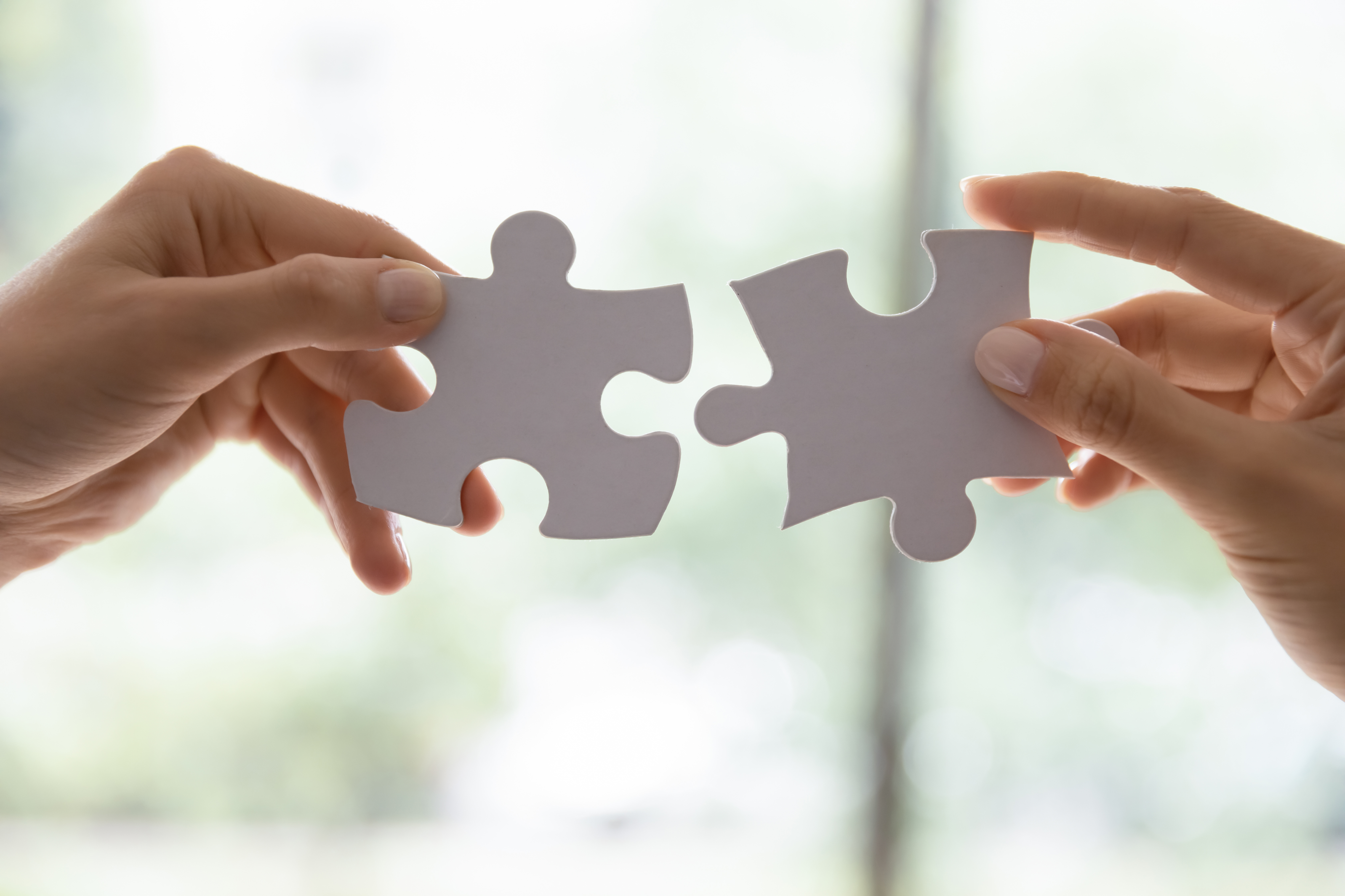 Close up photo of two hands trying to fit two large jigsaw pieces together 