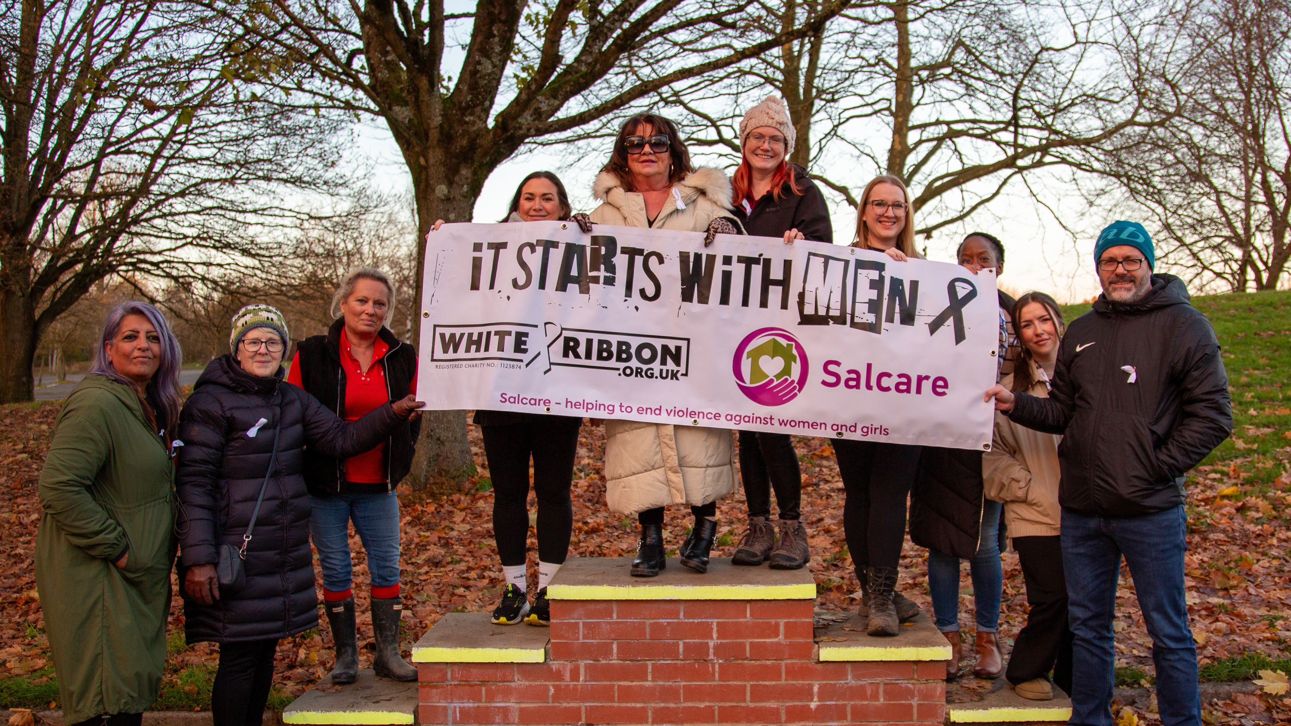 Photo of a group of people holding a banner that says 'It starts with Men - White Ribbon Day - Salcare'