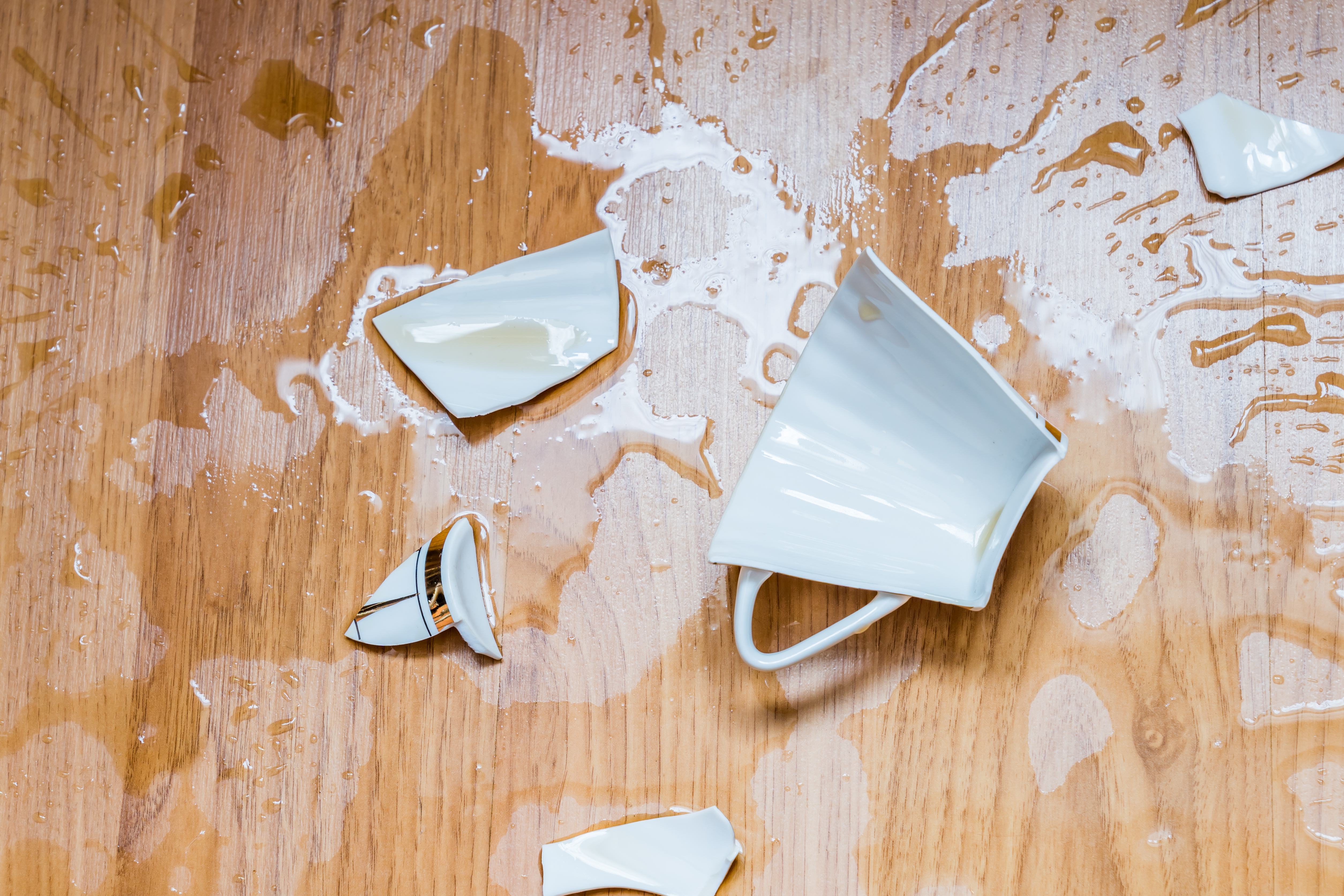 A broken tea cup on a wooden floor.