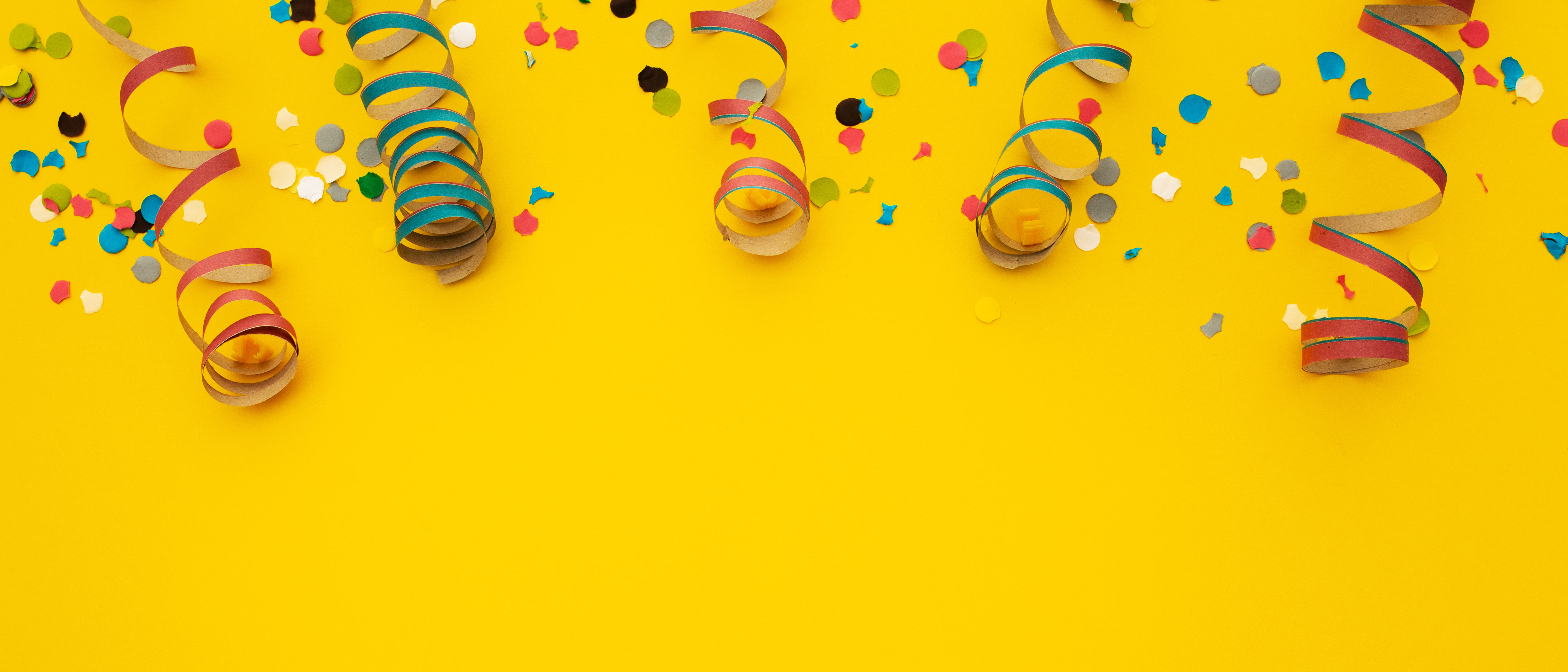 Different coloured spiralling steamers and paper confetti on a yellow surface