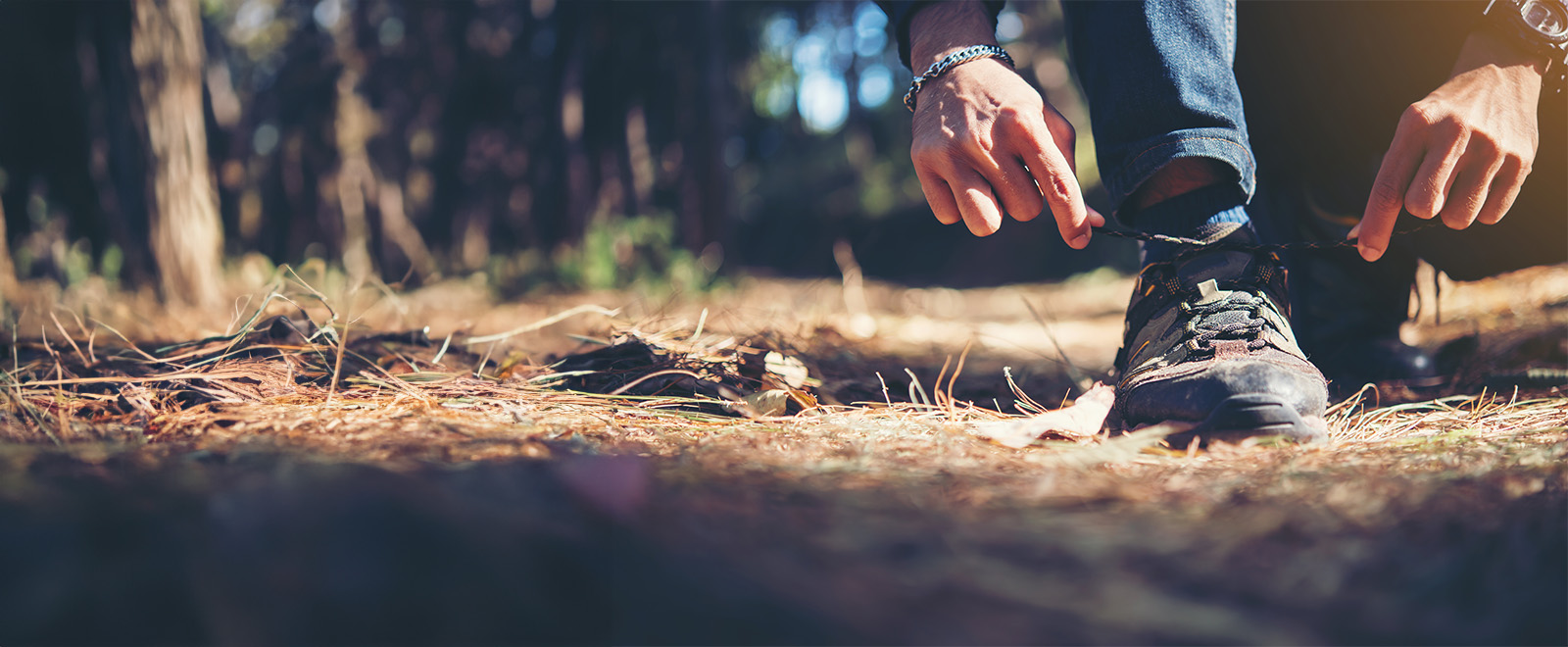 Man Tying Up Walking Shoes In A Forest Banner