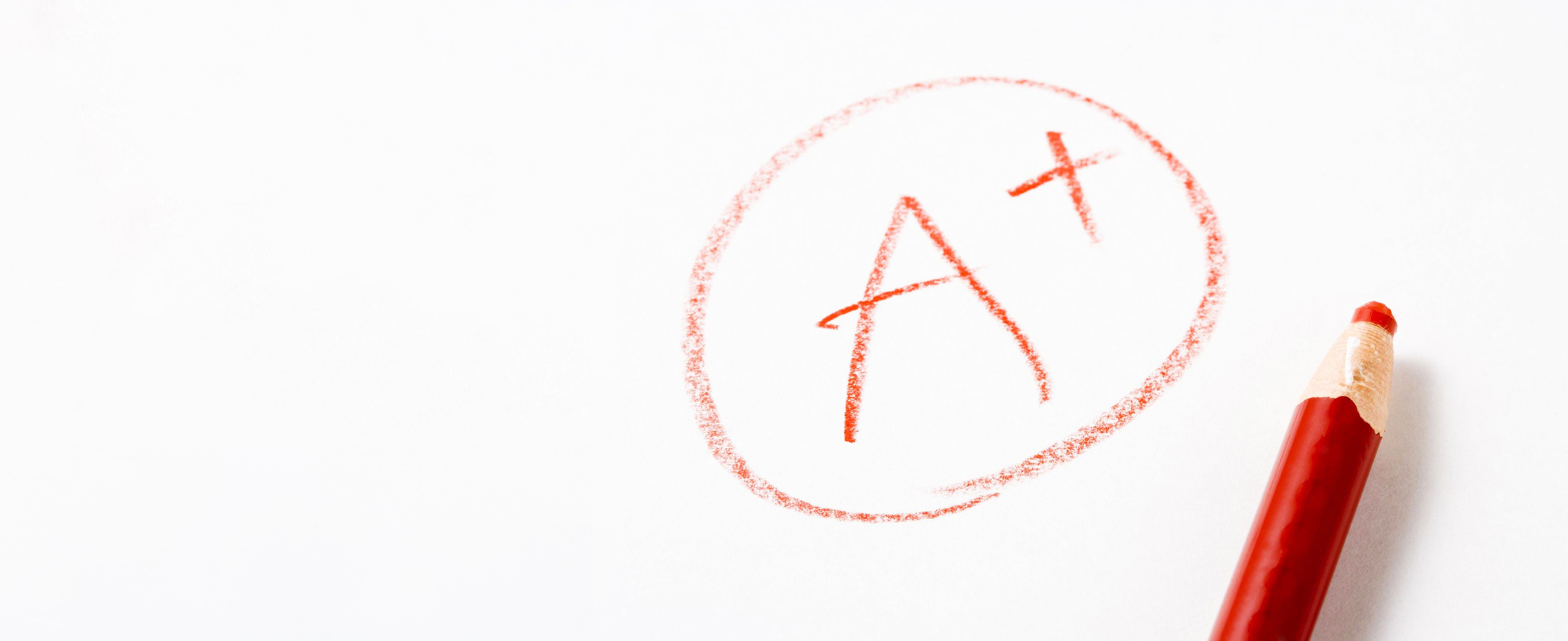 Photo of 'A+' written in red pencil on white paper with the pencil lying next to the writing
